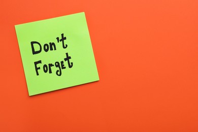 Photo of Paper note with phrase Don't Forget on orange background, top view. Space for text