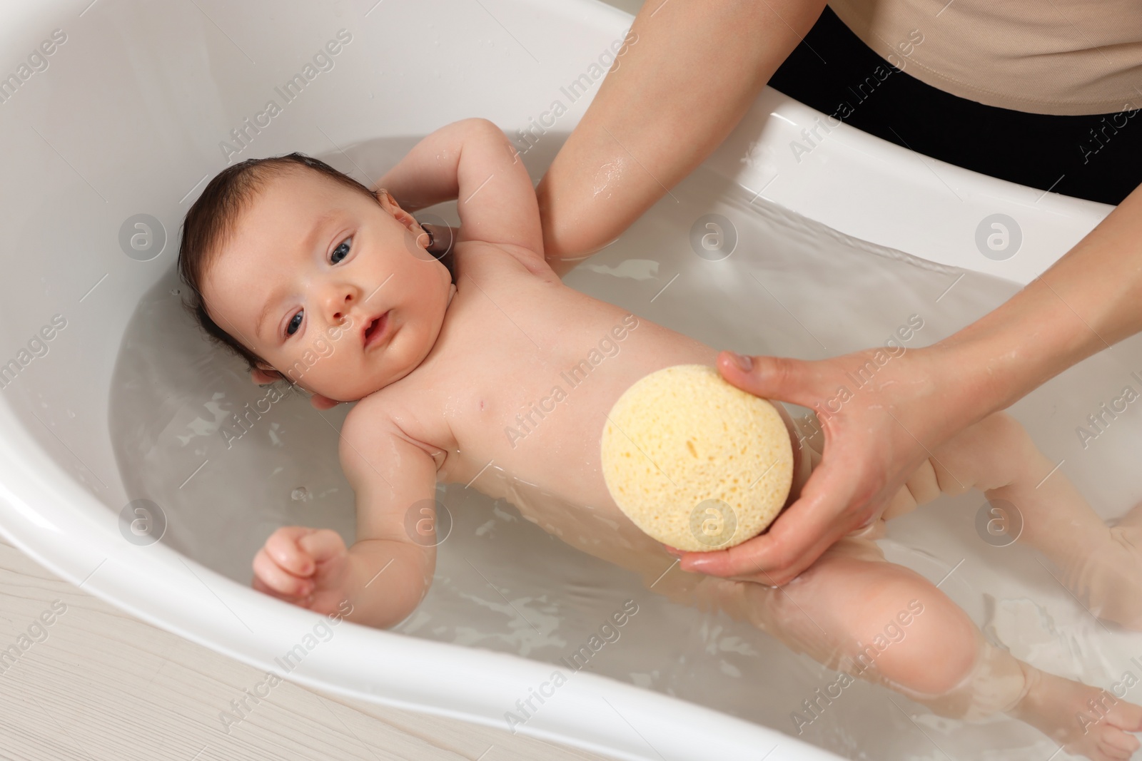 Photo of Mother bathing her little baby with sponge in bathtub, closeup