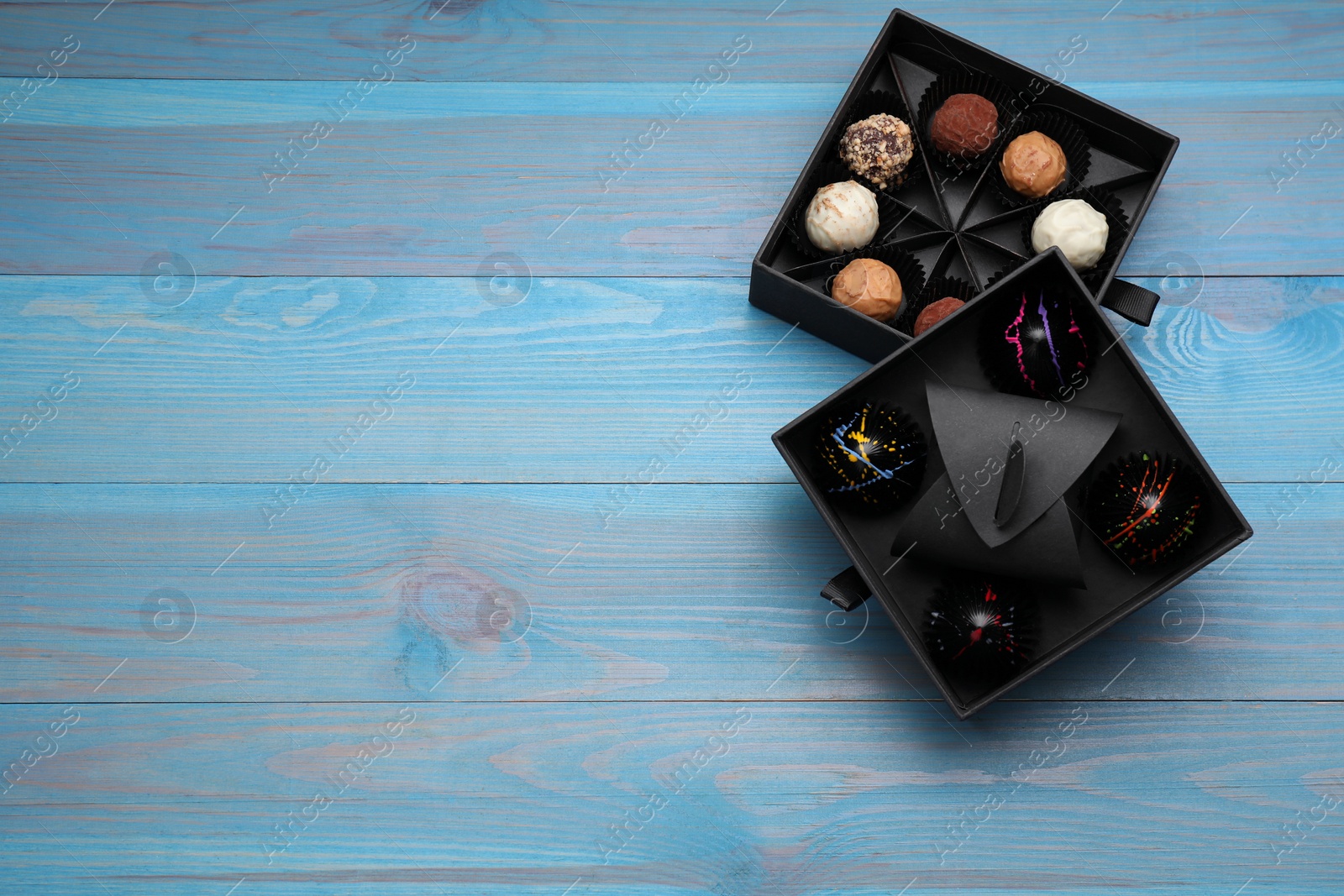 Photo of Boxes of tasty chocolate candies on light blue wooden table, flat lay. Space for text