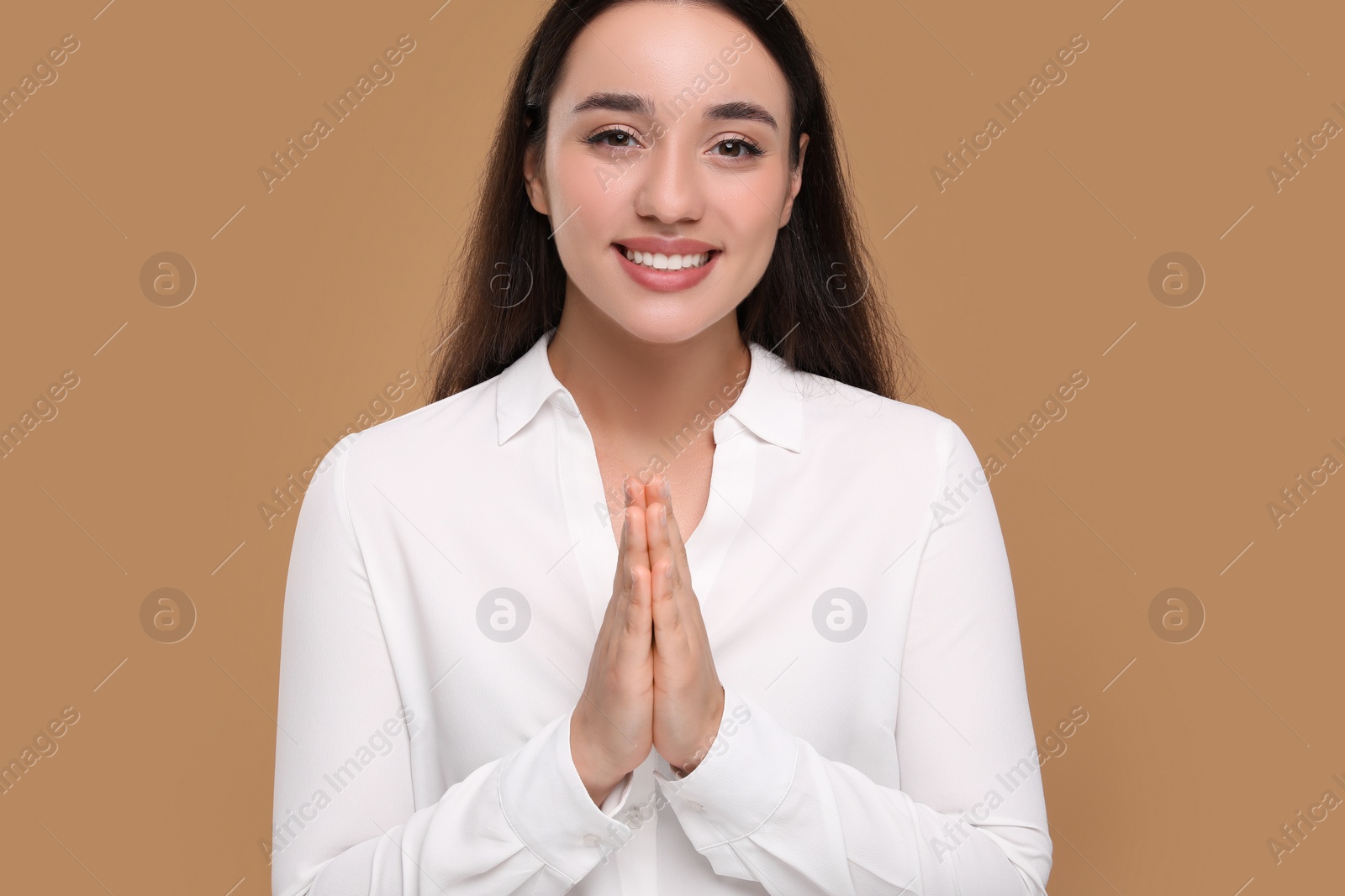 Photo of Thank you gesture. Beautiful grateful woman with hands clasped together on brown background