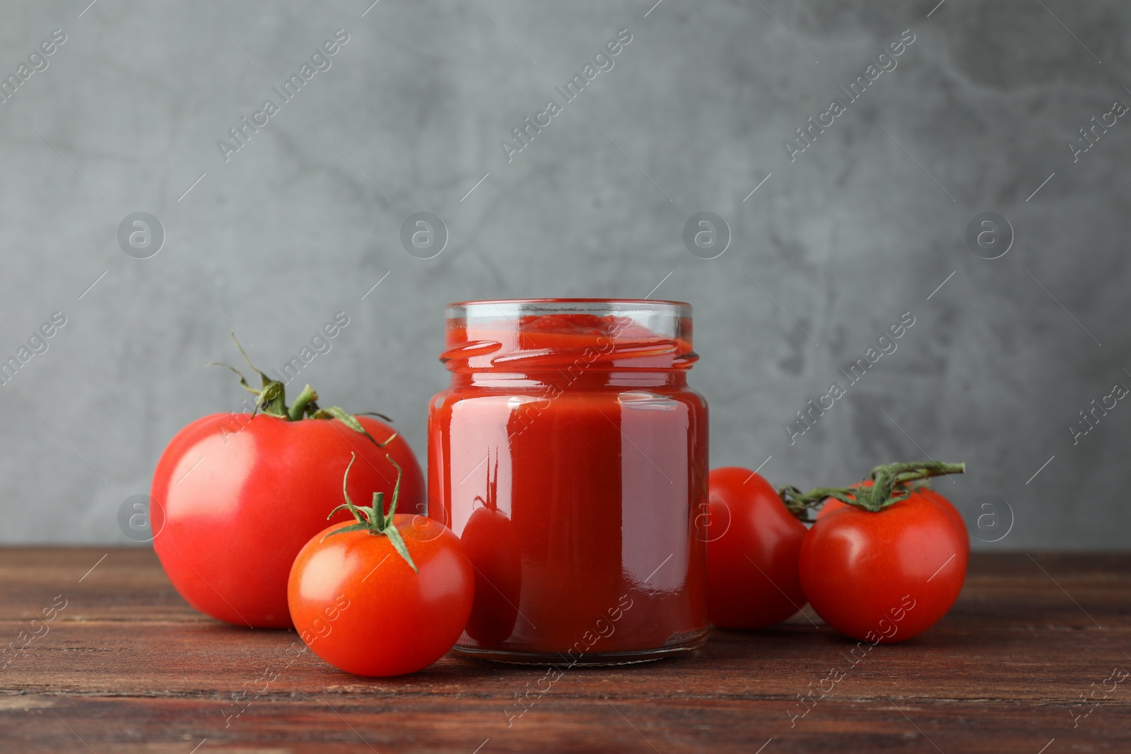 Photo of Jar of tasty ketchup and tomatoes on wooden table