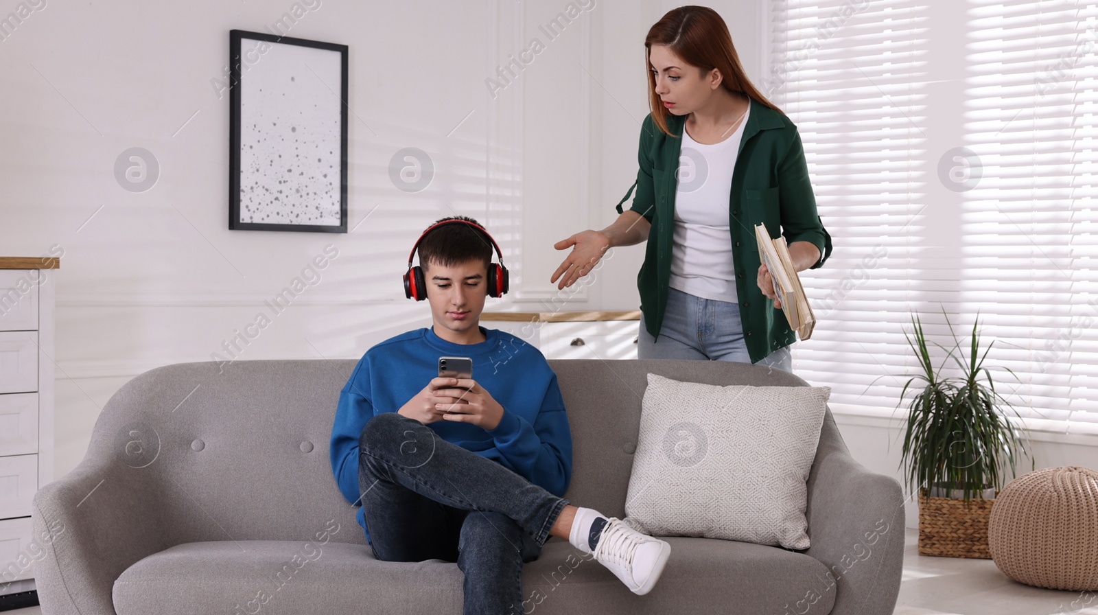 Photo of Strict mother with books scolding her son while he using smartphone at home. Teenager problems