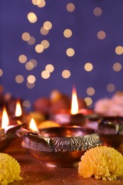 Photo of Diwali celebration. Diya lamps and chrysanthemum flowers on shiny golden table against blurred lights, closeup