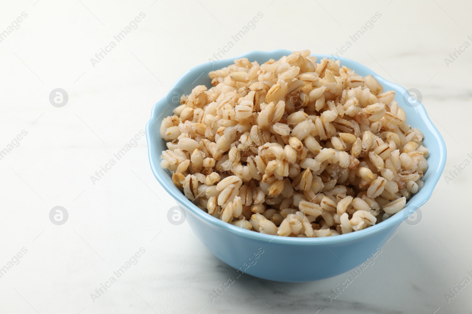 Photo of Delicious pearl barley in bowl on white marble table, closeup. Space for text