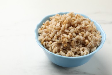 Photo of Delicious pearl barley in bowl on white marble table, closeup. Space for text