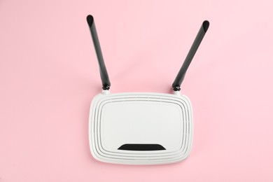 Modern Wi-Fi router on light pink background, top view