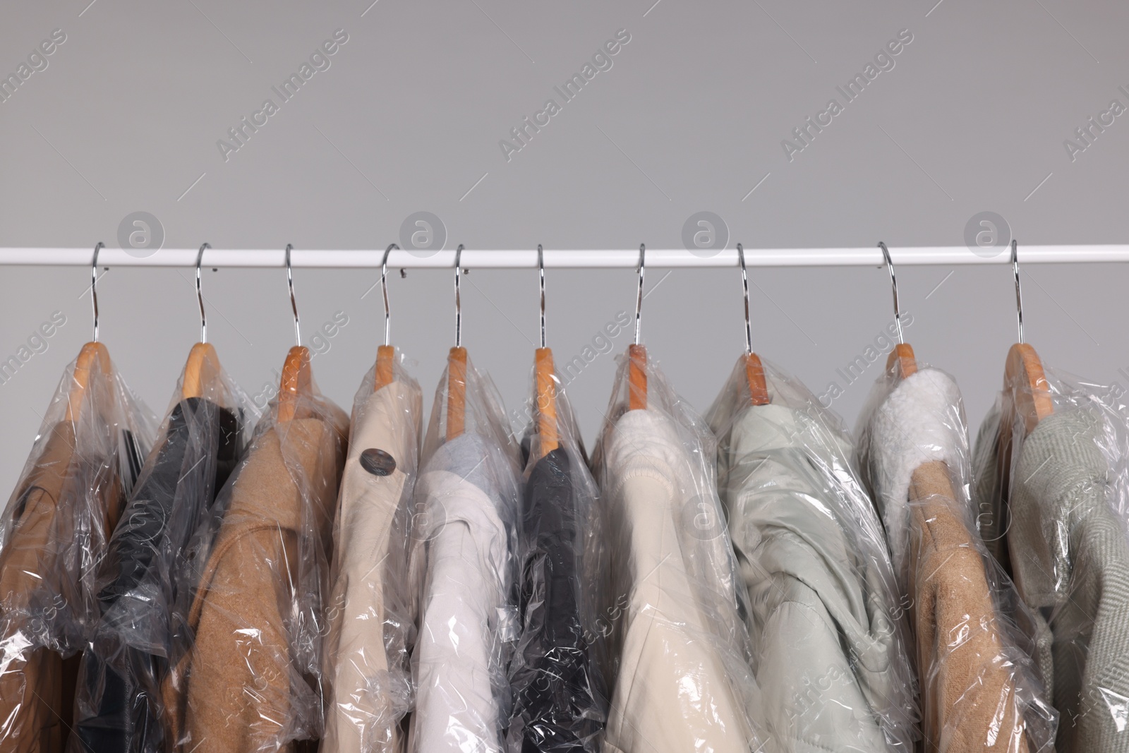 Photo of Dry-cleaning service. Many different clothes in plastic bags hanging on rack against grey background