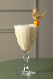 Photo of Refreshing cocktail decorated with physalis fruit on green table indoors