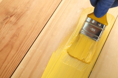 Photo of Worker applying yellow paint onto wooden surface, closeup. Space for text