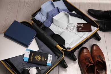 Open suitcase with men's clothes, accessories and shoes on floor