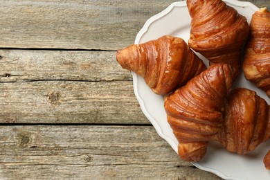 Plate with tasty croissants on wooden table, top view. Space for text
