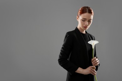 Photo of Sad woman with calla lily flower on grey background, space for text. Funeral ceremony