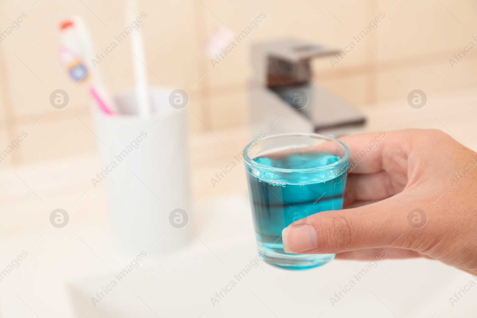 Photo of Woman holding glass with mouthwash for teeth and oral care in bathroom