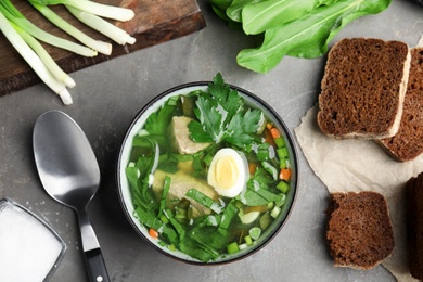 Delicious sorrel soup with meat and egg served on grey table, flat lay