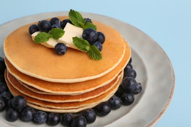 Stack of tasty pancakes with blueberries, butter and mint on light blue background, closeup