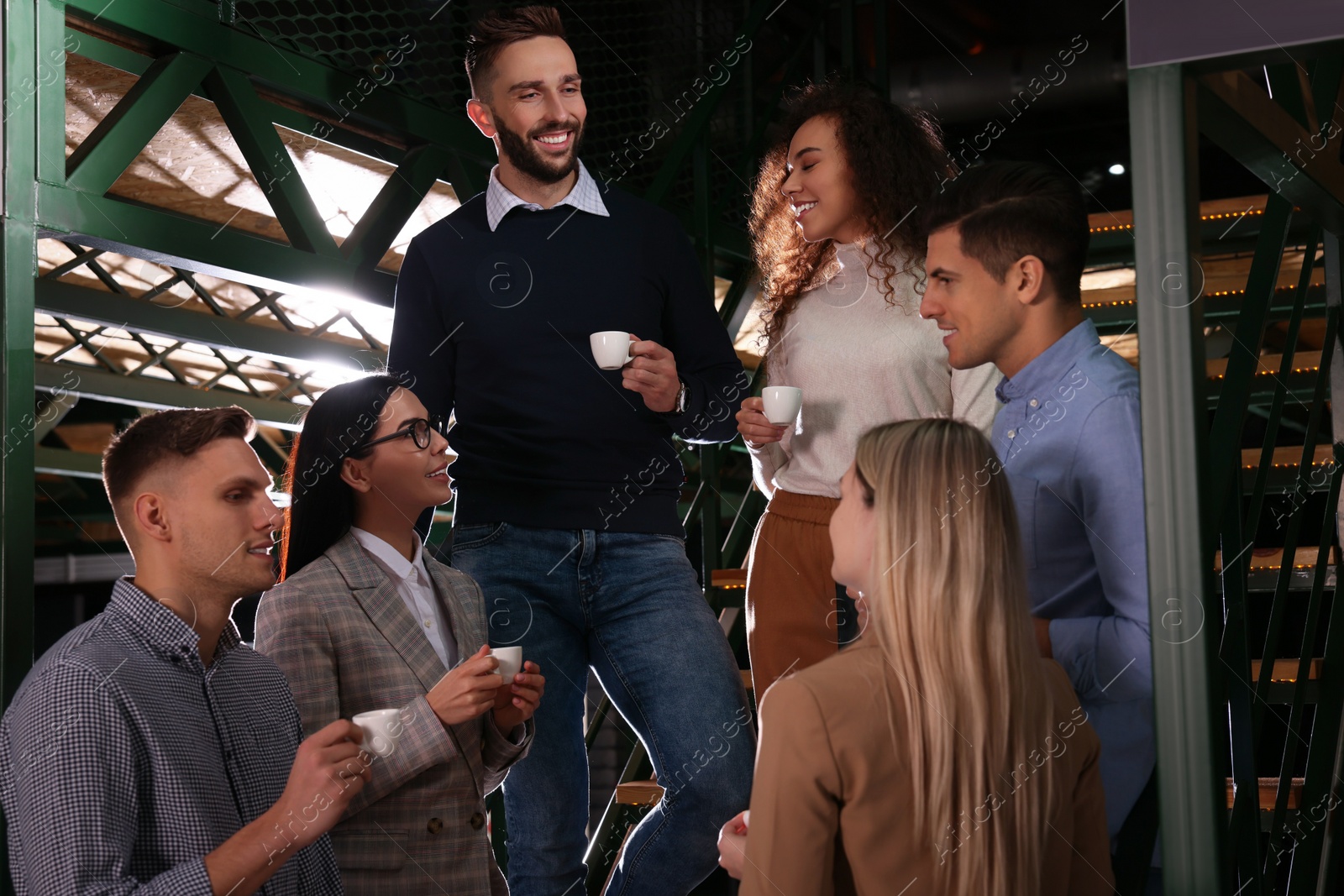 Photo of Group of coworkers talking during coffee break on stairs in office