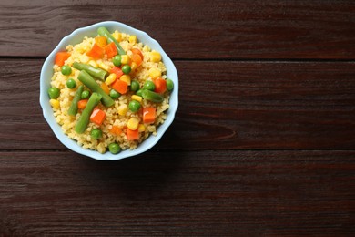 Photo of Tasty millet porridge with vegetables in bowl on wooden table, top view. Space for text