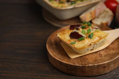 Photo of Spatula with piece of tasty sausage casserole on wooden table, closeup. Space for text