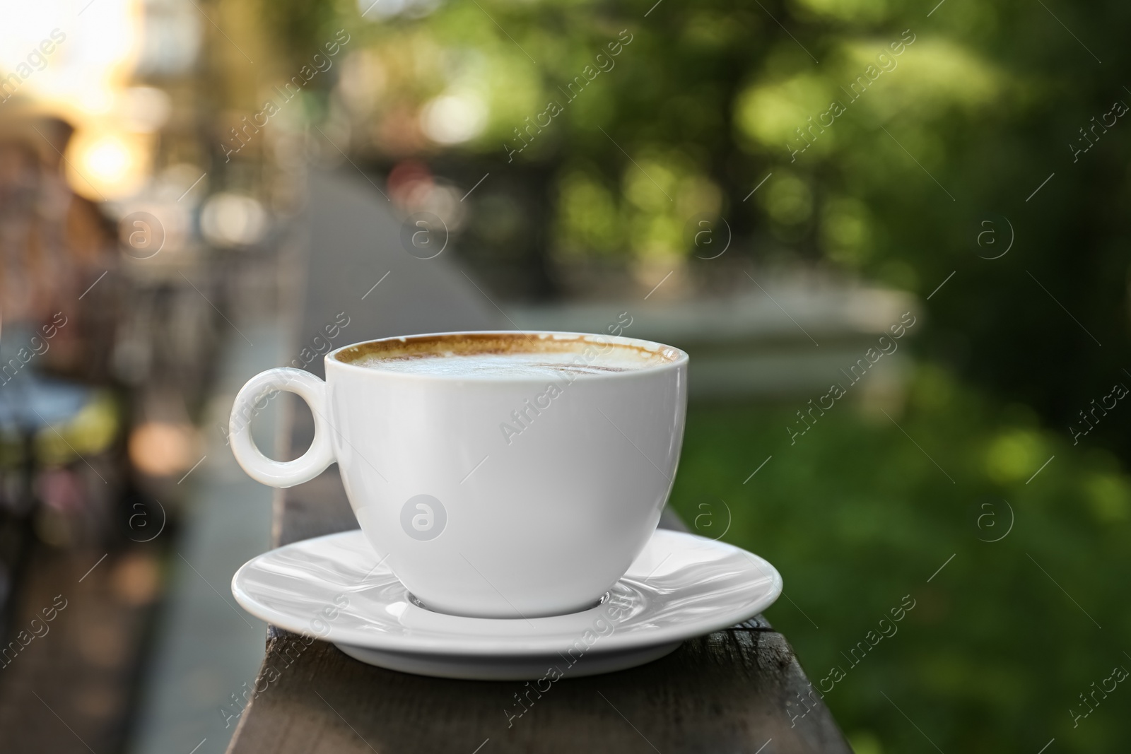 Photo of Cup of aromatic coffee on wooden railing outdoors