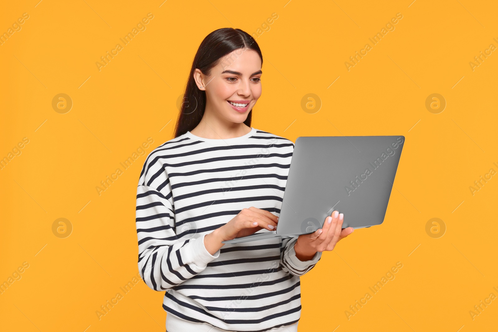 Photo of Happy woman using laptop on orange background