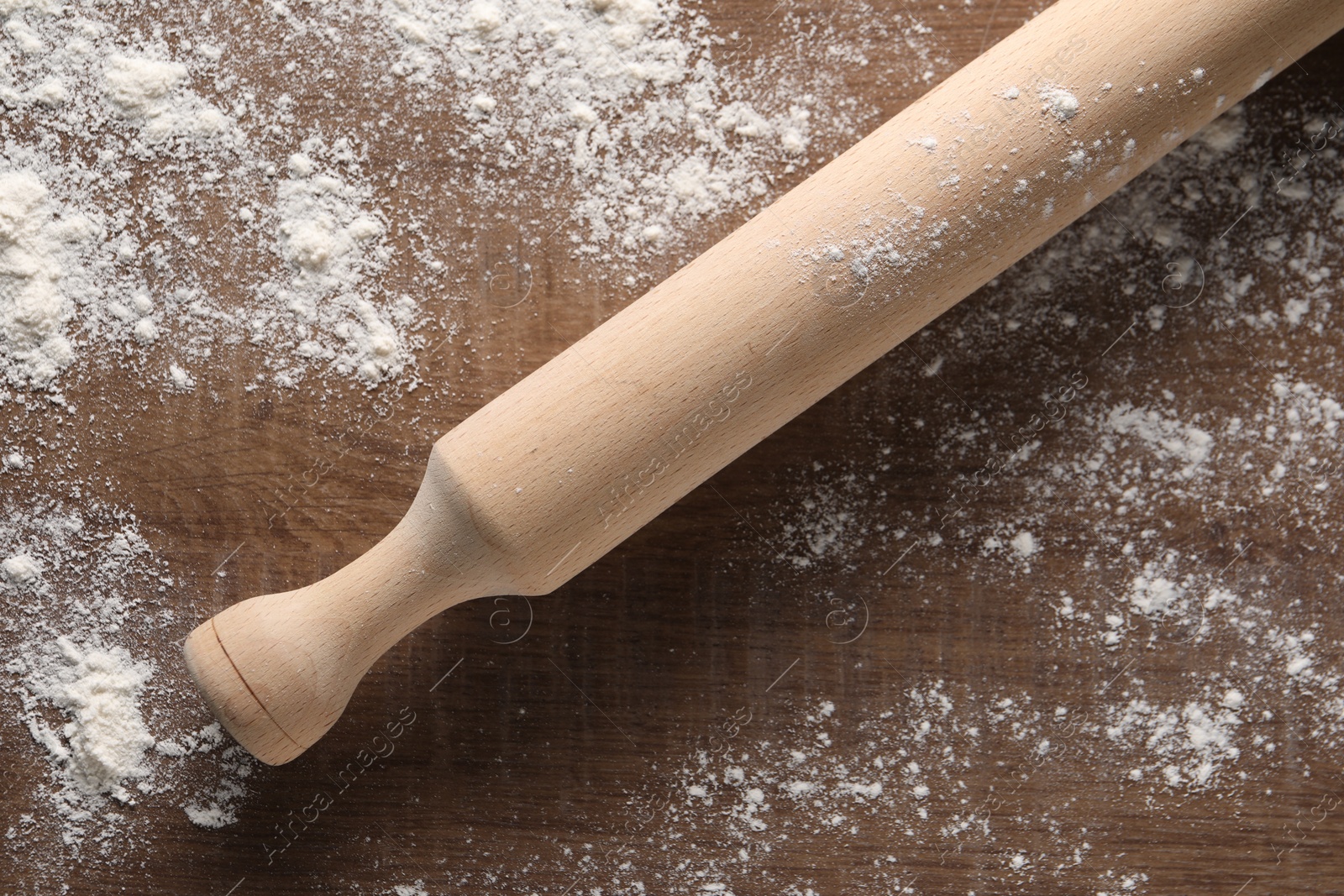 Photo of Scattered flour and rolling pin on wooden table, top view