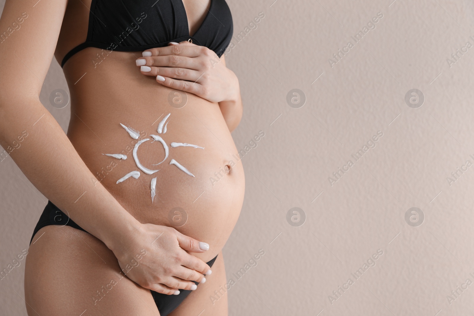 Photo of Pregnant woman with sun protection cream on her belly against beige background, closeup. Space for text