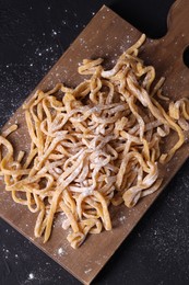 Board with homemade pasta and flour on dark table, top view