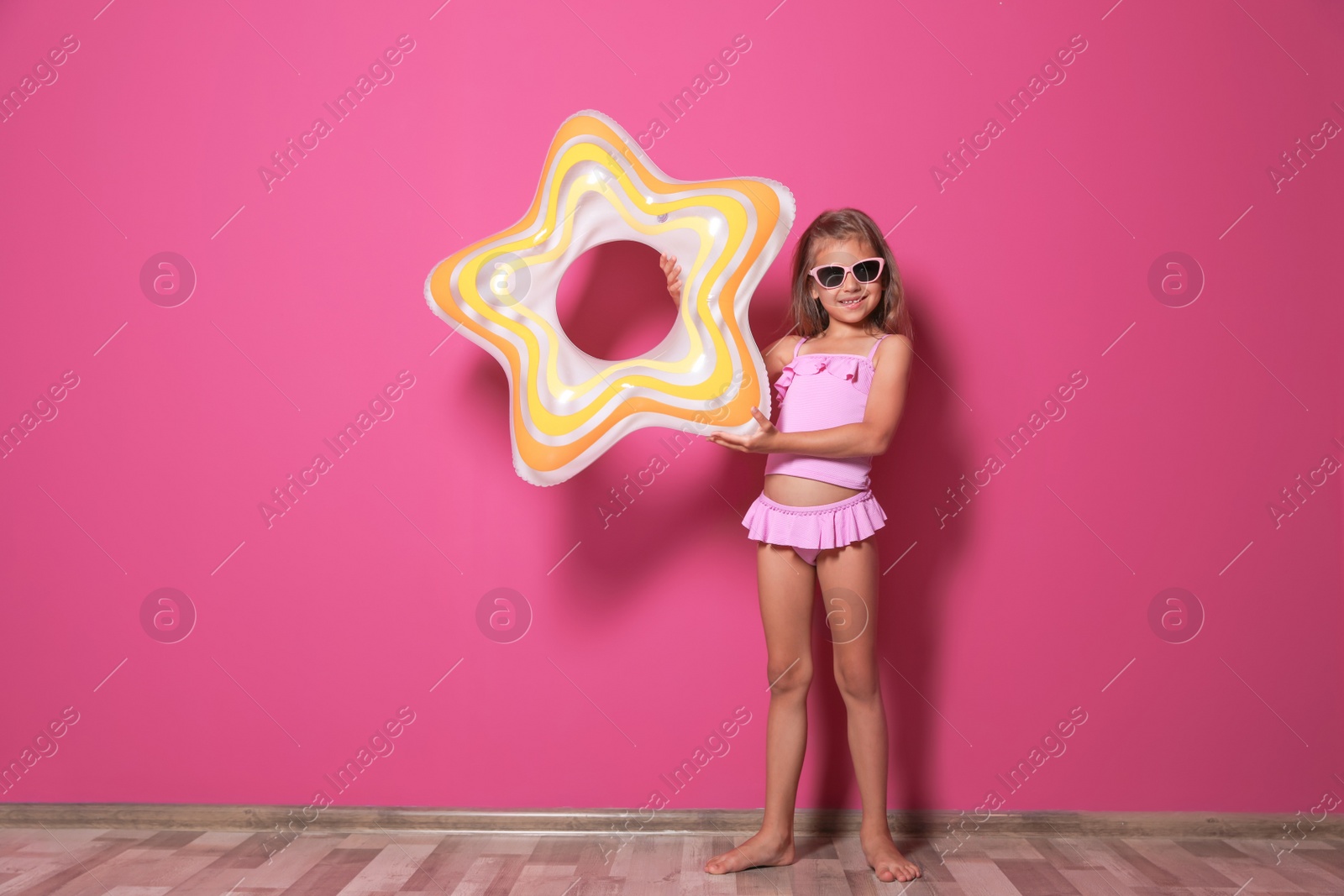 Photo of Cute little girl with bright star shaped inflatable ring near color wall