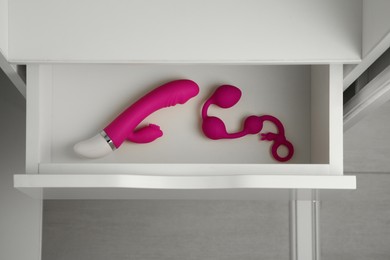 Photo of Pink vibrator and anal balls in open drawer of nightstand indoors, top view. Sex toys
