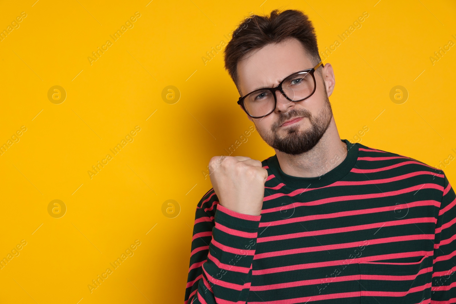 Photo of Aggressive man in striped sweatshirt and eyeglasses on yellow background, space for text