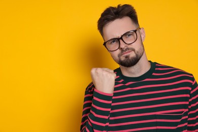 Photo of Aggressive man in striped sweatshirt and eyeglasses on yellow background, space for text