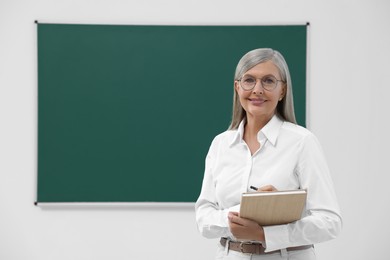 Photo of Portrait of professor with notebook near blackboard in classroom, space for text