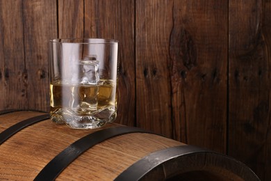 Photo of Whiskey with ice cubes in glass on barrel against wooden background, space for text