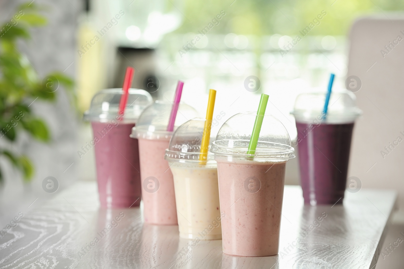 Photo of Different milk shakes in plastic cups on white wooden table indoors