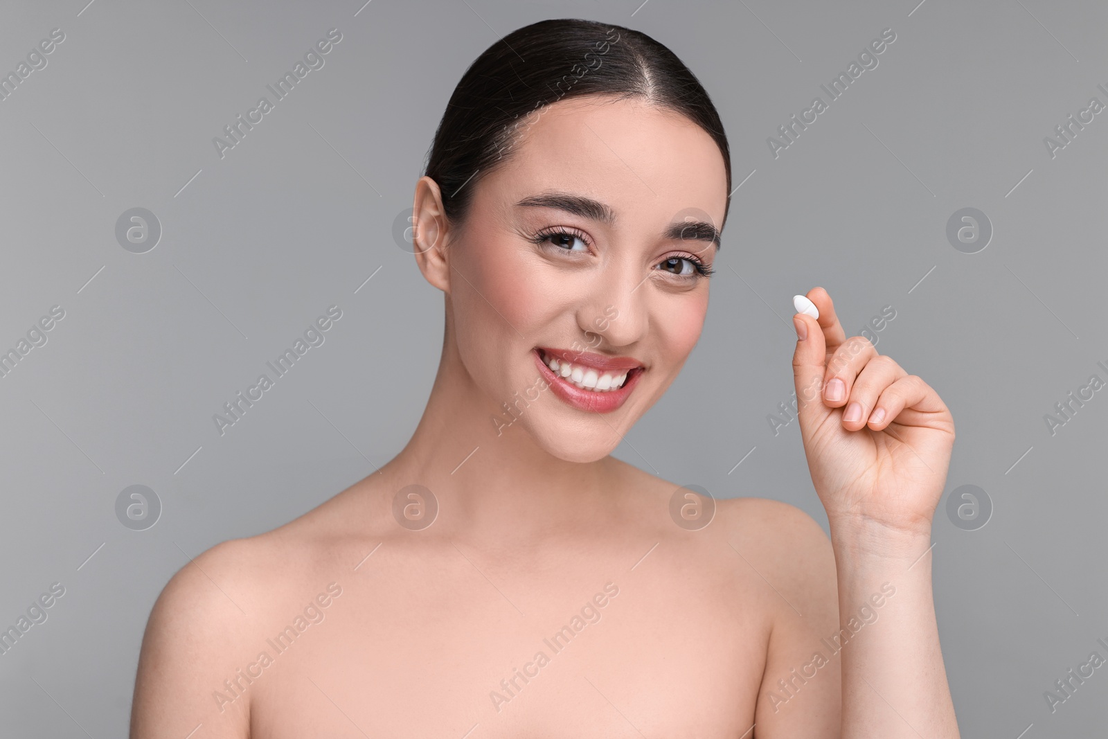 Photo of Beautiful young woman with vitamin pill on grey background