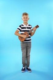 Little boy playing guitar on color background