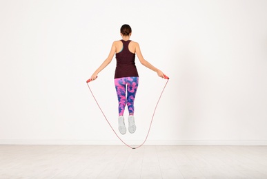 Sportive woman training with jump rope in light room