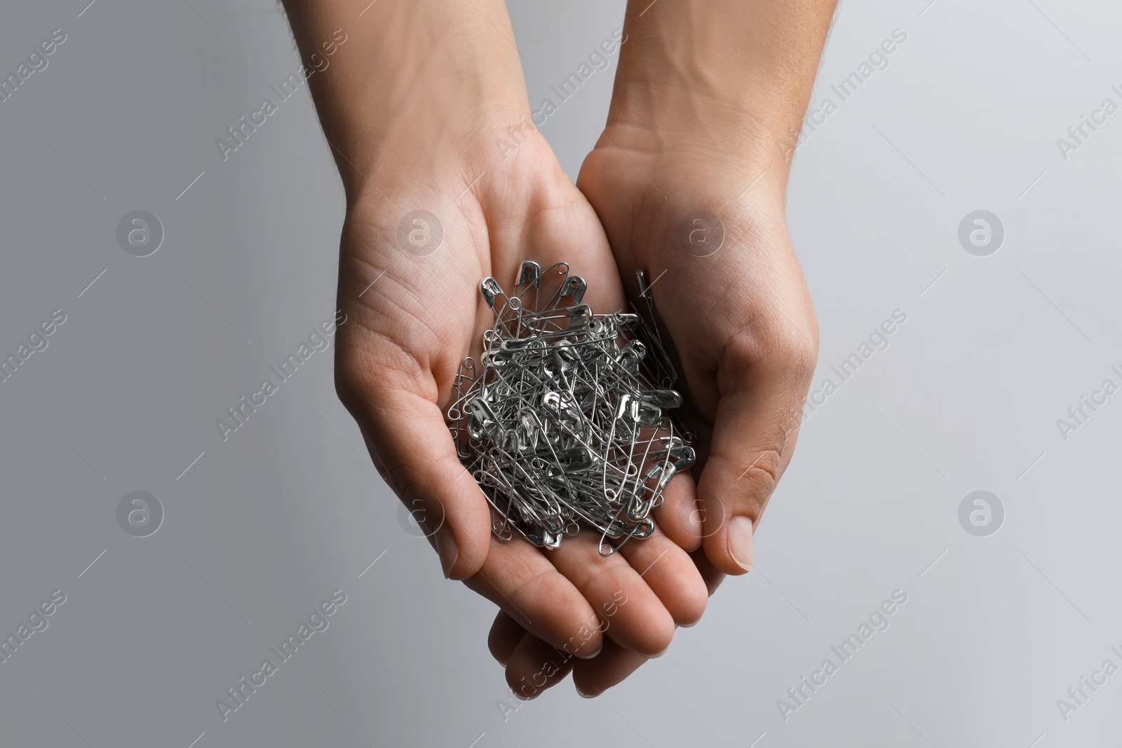 Photo of Woman holding pile of safety pins on light grey background, closeup