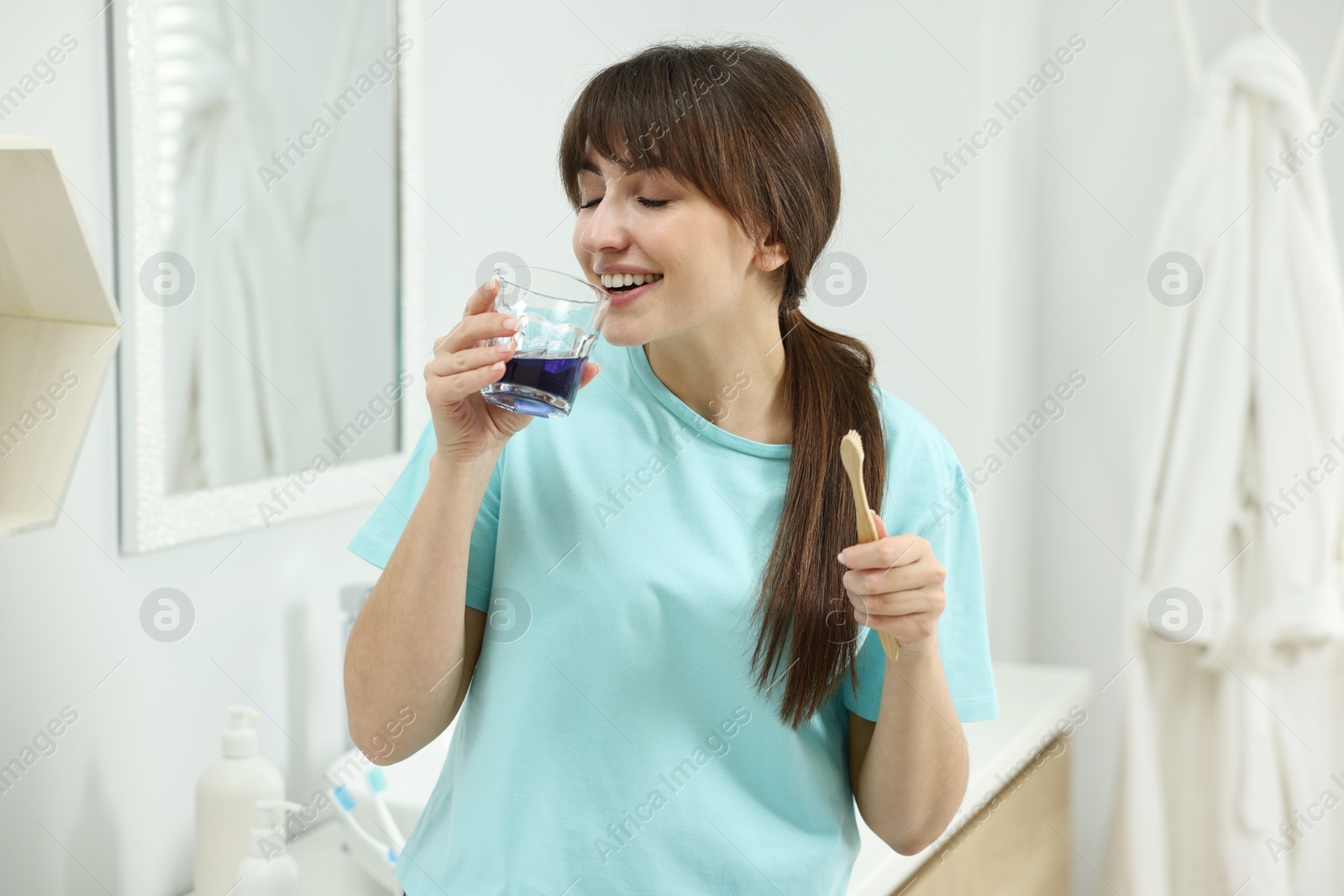 Photo of Young woman using mouthwash in bathroom. Oral hygiene