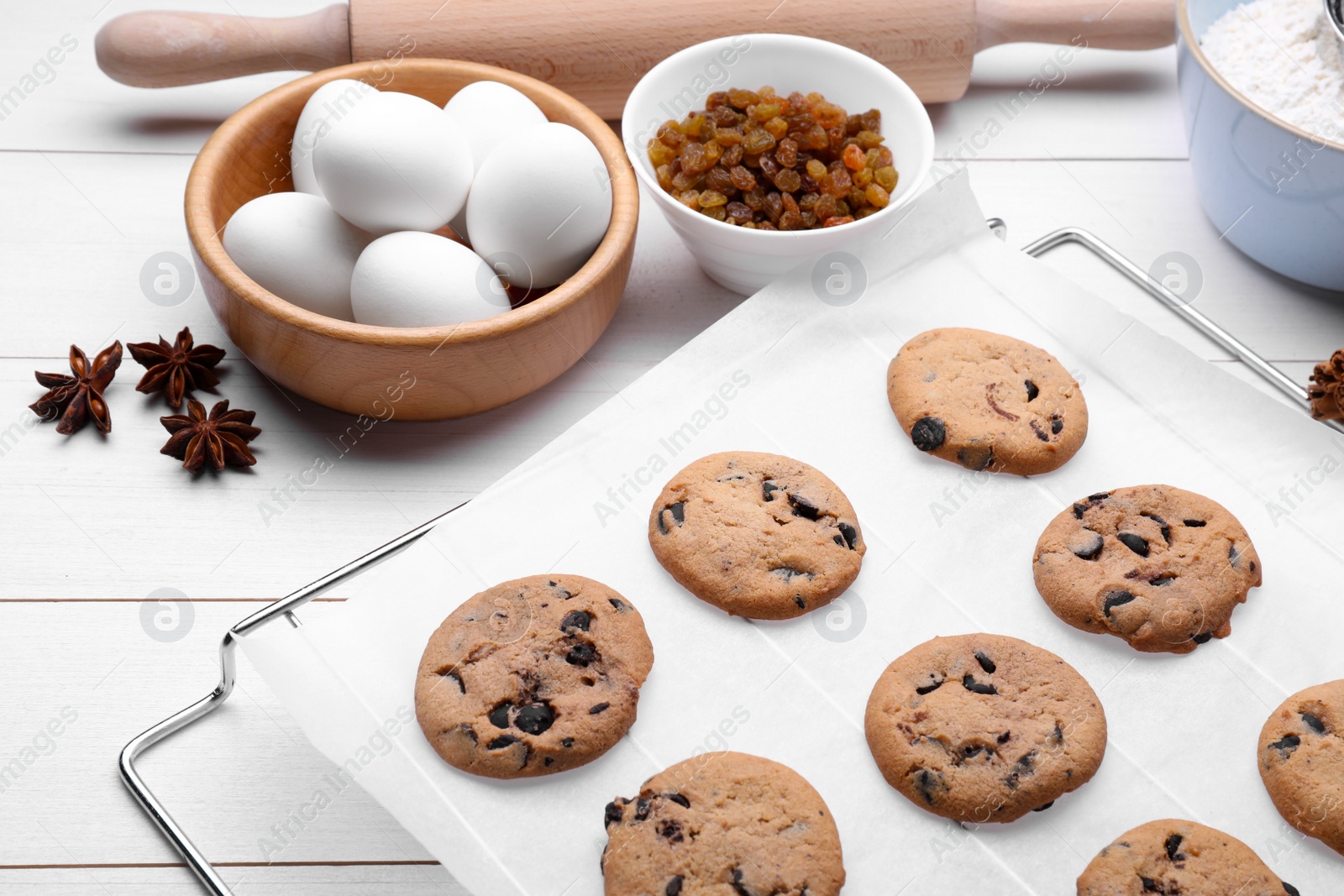 Photo of Cooling rack with parchment baking paper and tasty homemade cookies on white wooden table