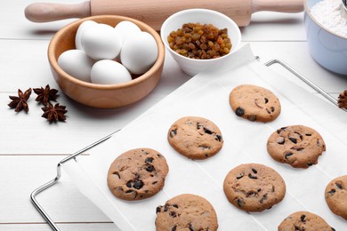 Cooling rack with parchment baking paper and tasty homemade cookies on white wooden table