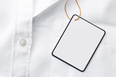 Photo of Cardboard tag with space for text on white shirt, top view