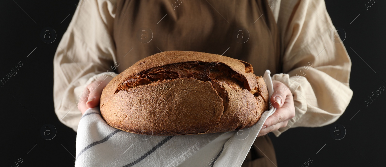 Photo of Woman holding freshly baked bread on black background, closeup