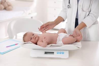 Photo of Doctor weighting cute baby in clinic, closeup. Health care