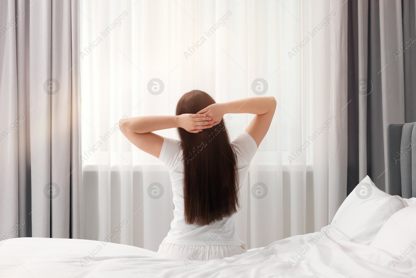 Photo of Woman stretching on bed at home, back view. Lazy morning