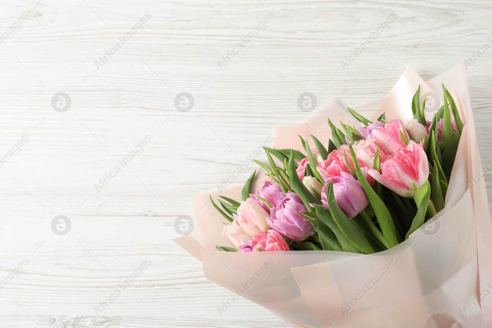 Photo of Bouquet of beautiful tulips on white wooden table, top view. Space for text