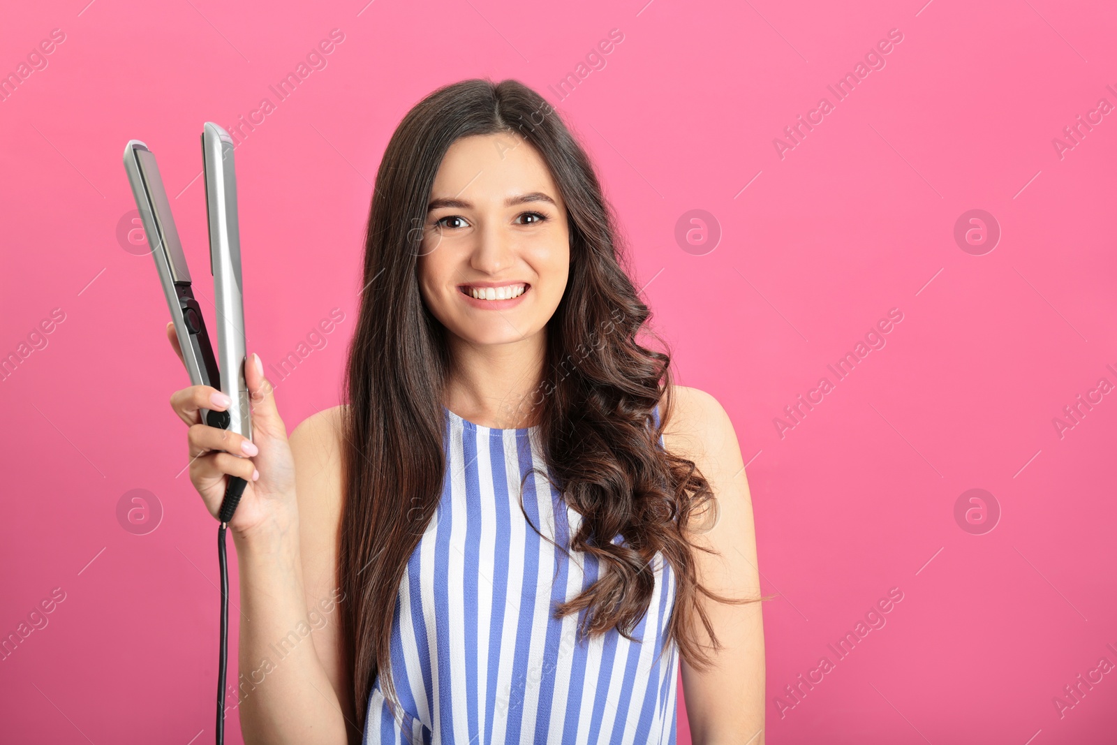 Photo of Young woman with modern hair iron on pink background, space for text