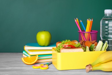 Photo of Lunch box with healthy food and different stationery on wooden table near green chalkboard, space for text