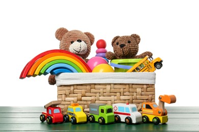 Photo of Wicker basket with different children's toys on green wooden table against white background