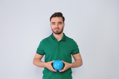 Young man with piggy bank on light background